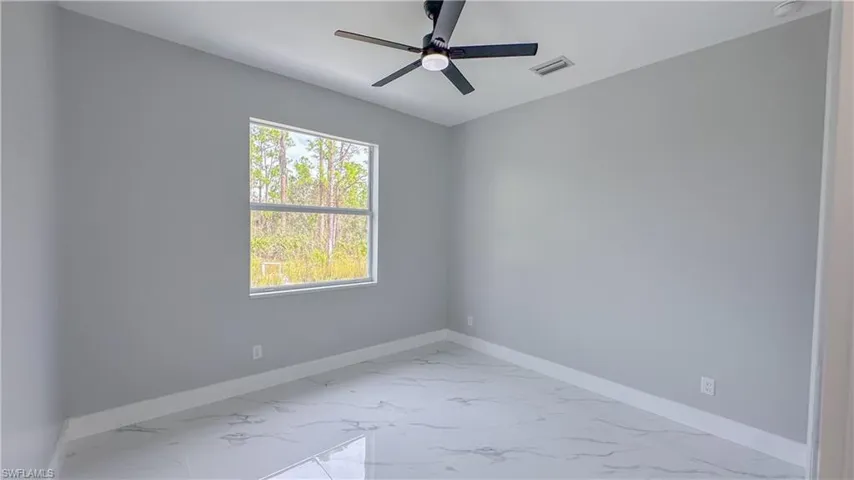 Empty room with baseboards, marble finish floor, visible vents, and a ceiling fan