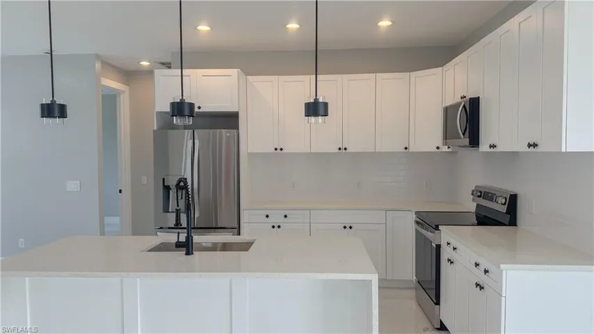 Kitchen with recessed lighting, backsplash, hanging light fixtures, white cabinets, and appliances with stainless steel finishes
