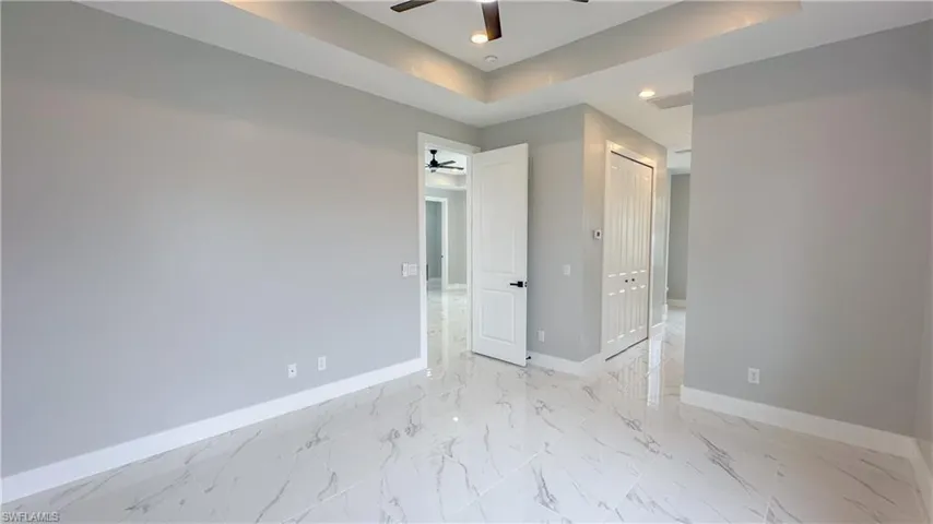 Unfurnished room featuring baseboards, marble finish floor, ceiling fan, recessed lighting, and a tray ceiling