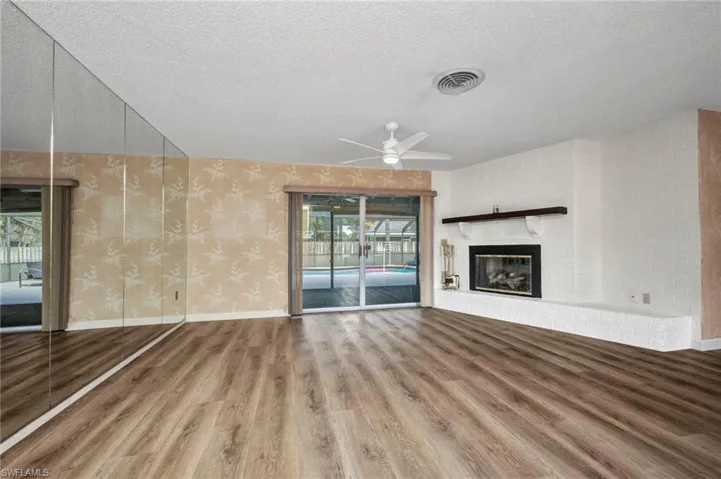 Unfurnished living room featuring wood finished floors, a ceiling fan, wallpapered walls, a textured ceiling, and a fireplace