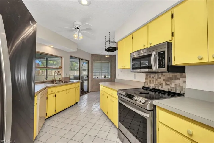 Kitchen with stainless steel appliances, a sink, a ceiling fan, light tile patterned floors, and backsplash