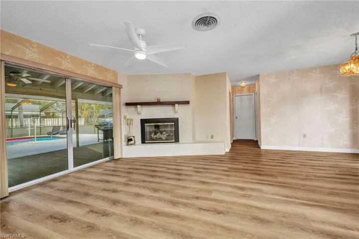 Unfurnished living room featuring ceiling fan, light wood finished floors, a brick fireplace, wallpapered walls, and a textured ceiling