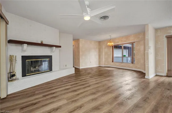 Unfurnished living room featuring a ceiling fan, wood finished floors, a chandelier, a brick fireplace, and a textured ceiling