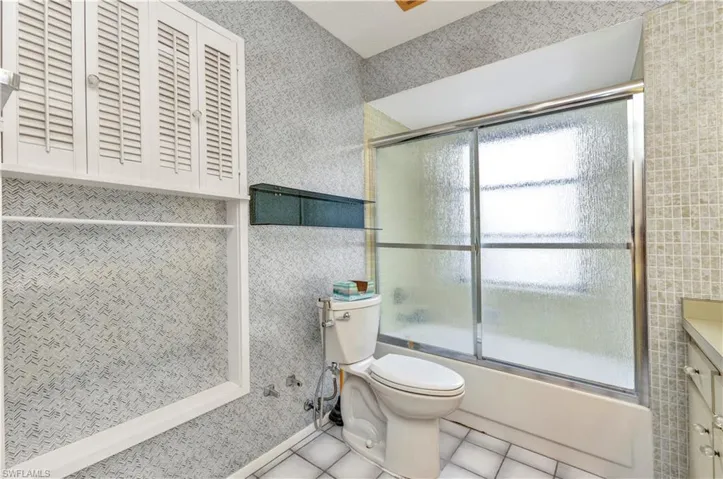 Full bath featuring toilet, tile patterned floors, bath / shower combo with glass door, vanity, and tile walls