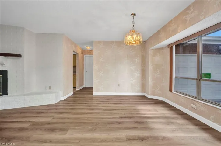 Unfurnished dining area featuring wood finished floors, a chandelier, baseboards, a brick fireplace, and wallpapered walls