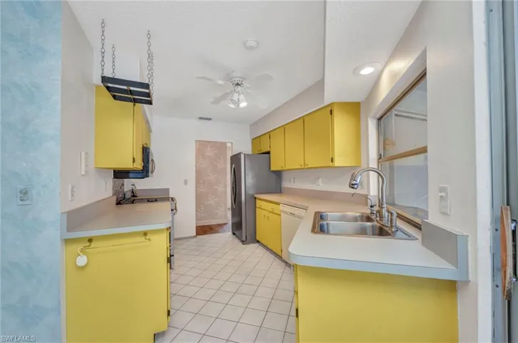 Kitchen with a sink, stainless steel appliances, ceiling fan, light countertops, and light tile patterned floors