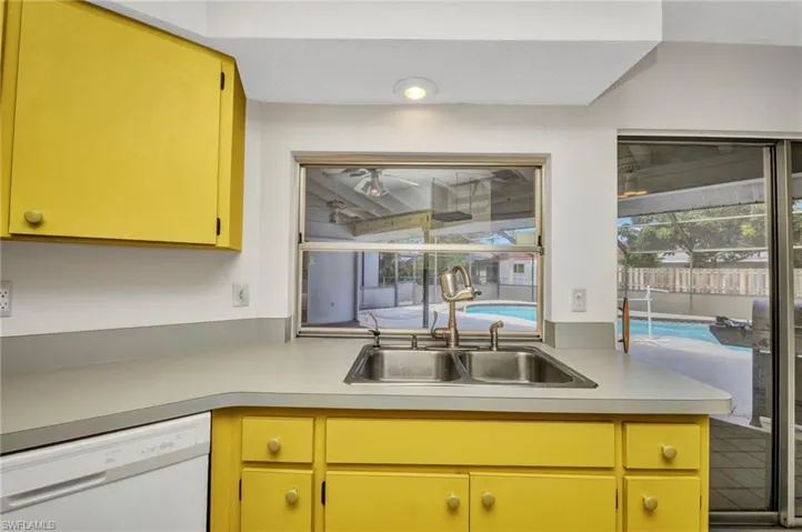 Kitchen with dishwasher, light countertops, a sink, and yellow cabinets