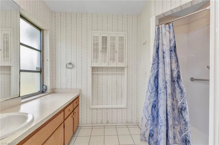 Bathroom with vanity, wallpapered walls, tile patterned flooring, and curtained shower