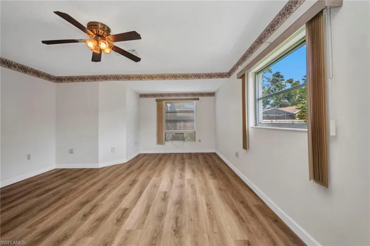 Empty room with light wood finished floors, baseboards, a ceiling fan, and cooling unit