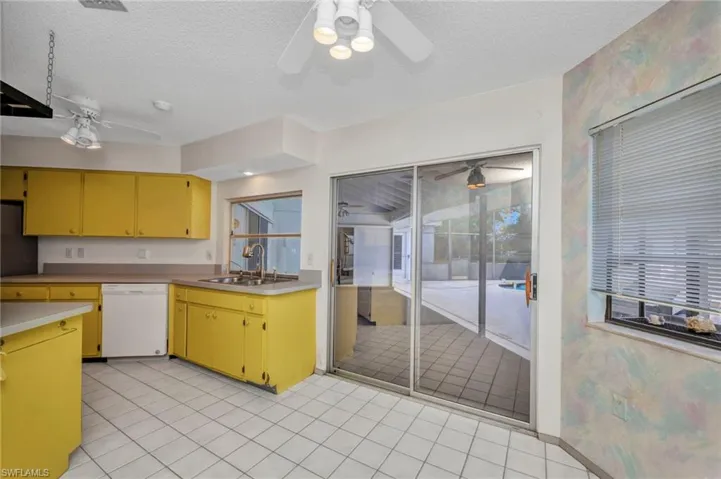 Kitchen with dishwasher, a sink, ceiling fan, a textured ceiling, and yellow cabinets