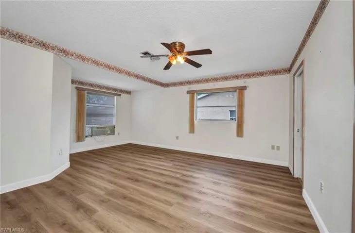 Empty room featuring ceiling fan, a textured ceiling, baseboards, wood finished floors, and cooling unit