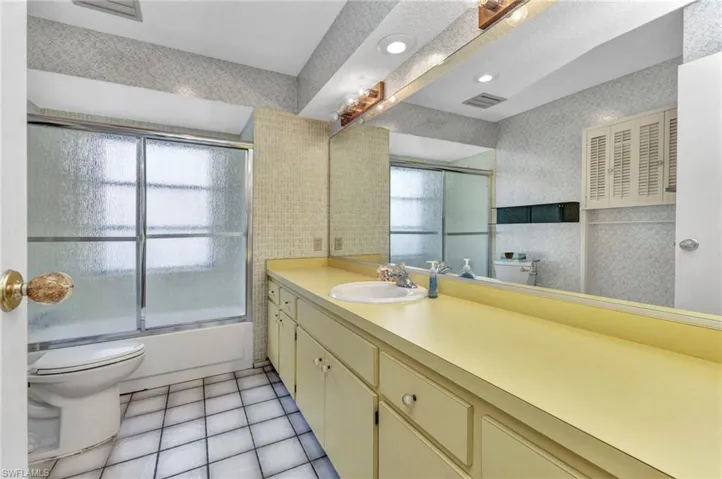 Full bath featuring toilet, vanity, shower / bath combination with glass door, tile patterned floors, and tile walls