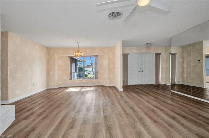 Unfurnished living room featuring wallpapered walls, wood finished floors, baseboards, a chandelier, and a ceiling fan
