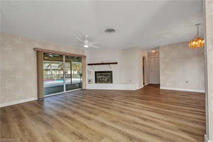 Unfurnished living room featuring wallpapered walls, wood finished floors, ceiling fan, a textured ceiling, and baseboards