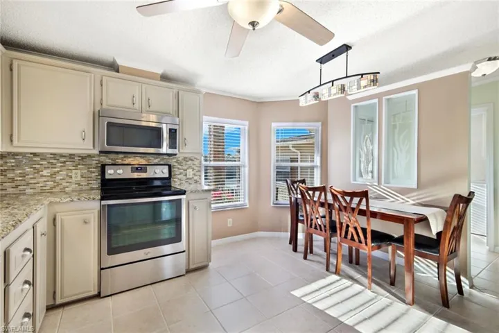 Kitchen featuring cream cabinets, stainless steel appliances, crown molding, decorative backsplash, and light tile patterned floors