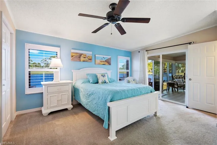 Carpeted bedroom featuring a textured ceiling, multiple windows, access to outside, ceiling fan, and vaulted ceiling