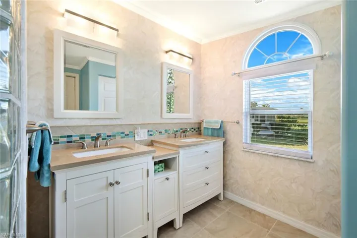 Full bath with plenty of natural light, ornamental molding, two vanities, light tile patterned flooring, and wallpapered walls