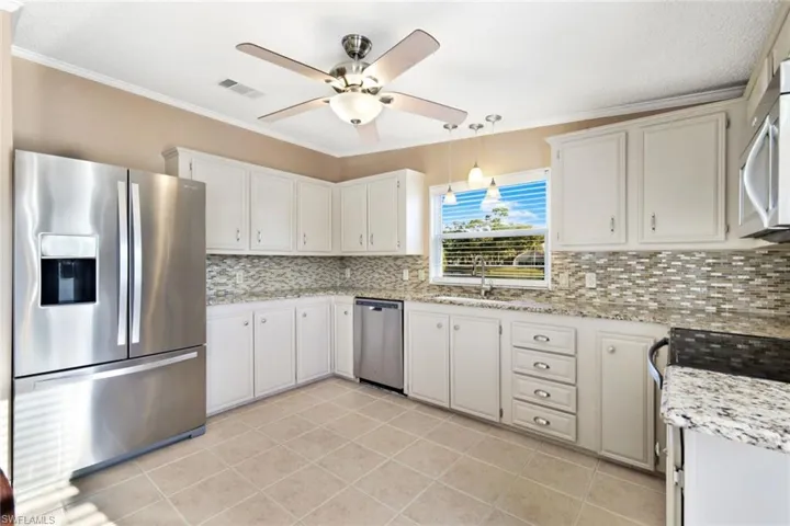 Kitchen with stainless steel appliances, crown molding, decorative light fixtures, light stone counters, and ceiling fan