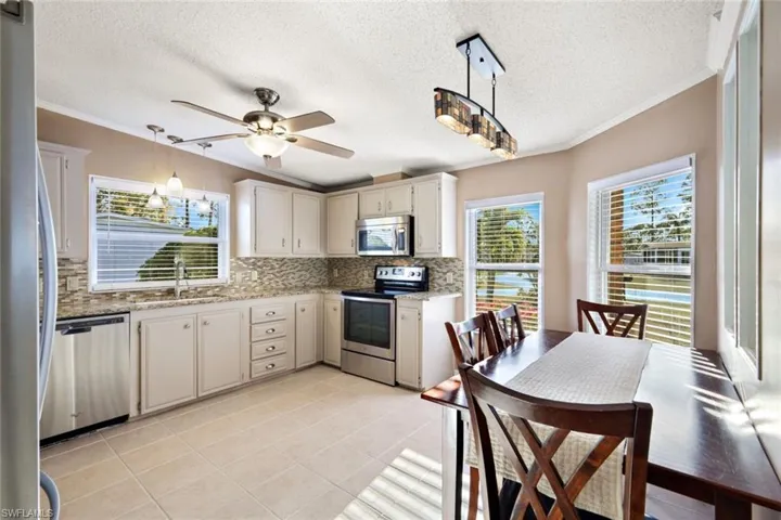 Kitchen featuring crown molding, hanging light fixtures, stainless steel appliances, plenty of natural light, and light stone counters