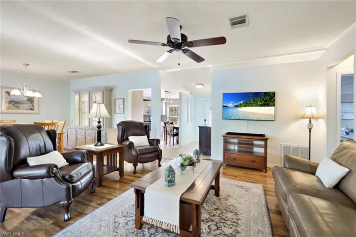 Living room with a chandelier, a textured ceiling, wood finished floors, a ceiling fan, and crown molding