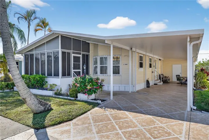 Manufactured / mobile home featuring an attached carport, a sunroom, a front yard, and entry steps