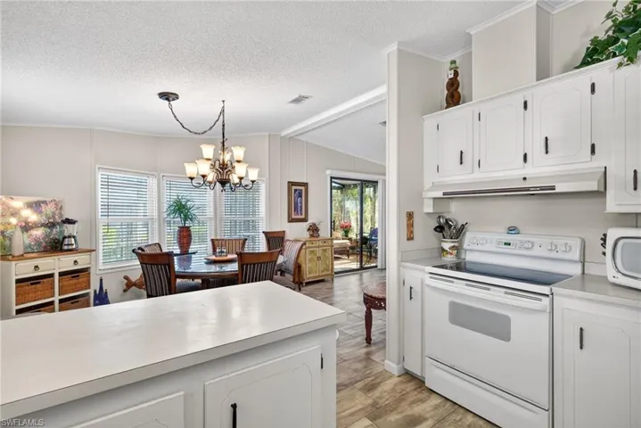 Kitchen featuring white appliances, white cabinets, light countertops, a chandelier, and lofted ceiling
