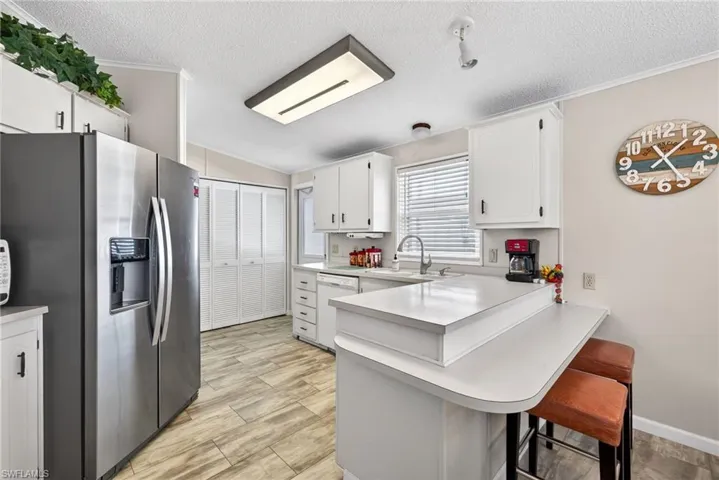 Kitchen featuring stainless steel fridge, light countertops, white cabinets, a breakfast bar, and a peninsula