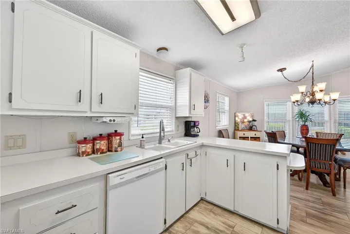 Kitchen with a peninsula, light countertops, dishwasher, white cabinets, and a chandelier