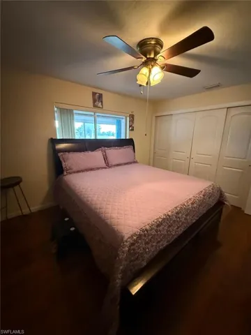 Wood-finish flooring, ceiling fan with integrated lighting, multi-panel sliding closet doors, and horizontal window