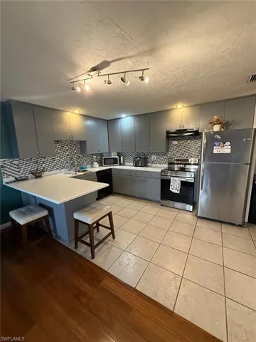 Kitchen featuring gray cabinetry, stainless steel appliances, a white countertop peninsula, a geometric tile backsplash, and ceramic tile flooring