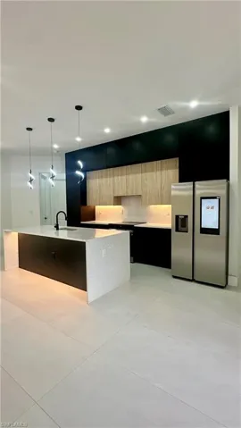 Kitchen featuring modern cabinets, stainless steel fridge with ice dispenser, a sink, light brown cabinets, and an island with sink