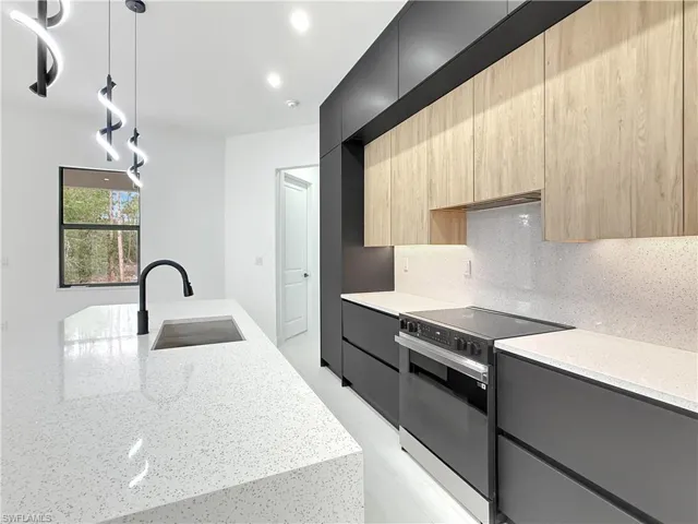 Kitchen with electric range oven, modern cabinets, a sink, light brown cabinets, and light stone countertops
