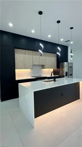 Kitchen with modern cabinets, a sink, stainless steel fridge, a large island with sink, and tasteful backsplash