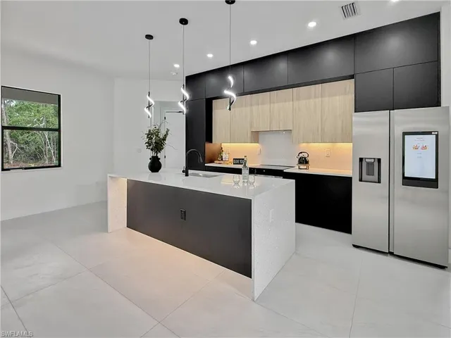Kitchen with stainless steel fridge, dark cabinetry, a sink, modern cabinets, and a kitchen island with sink