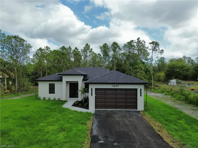 Prairie-style home with driveway, a shingled roof, a front lawn, and stucco siding