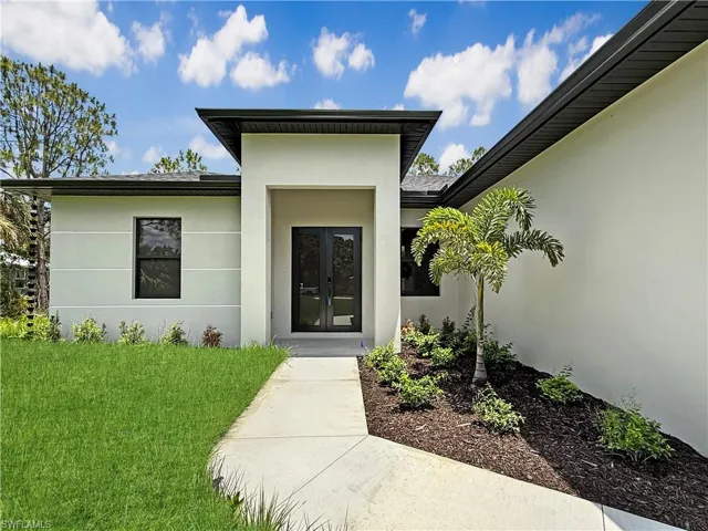 Property entrance with stucco siding, french doors, and a lawn