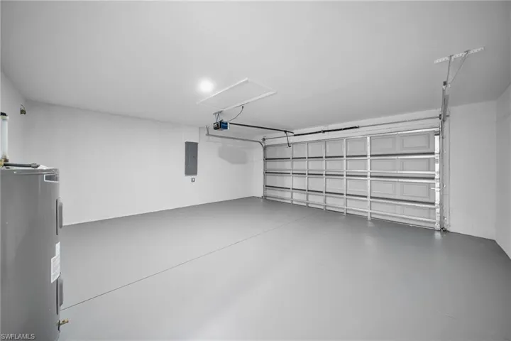 Garage with electric water heater, electric panel, and a garage door opener