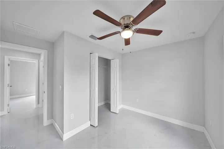Unfurnished bedroom with light marble finish floors, attic access, a closet, and ceiling fan