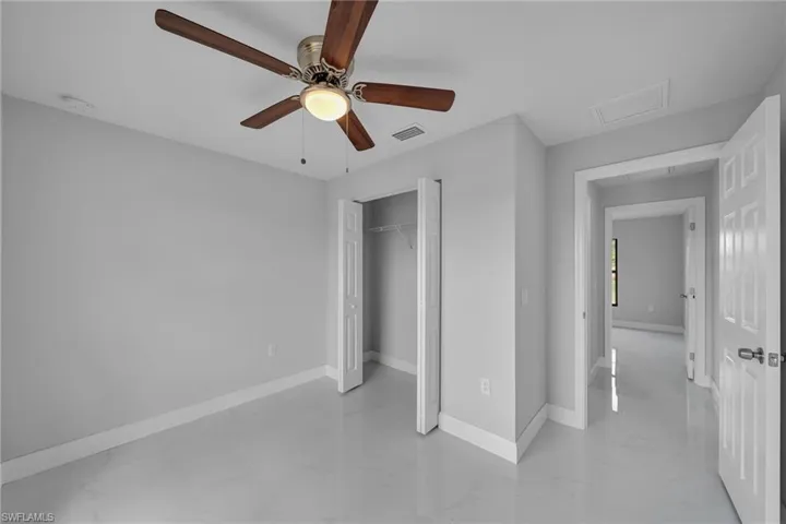 Unfurnished bedroom featuring attic access, a closet, light marble finish floors, and a ceiling fan