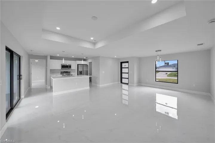 Unfurnished living room with recessed lighting, light marble finish flooring, and a raised ceiling