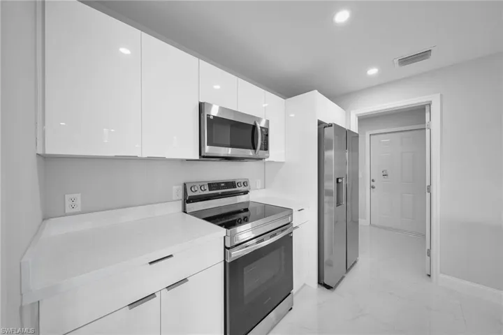 Kitchen with stainless steel appliances, modern cabinets, white cabinetry, light countertops, and light marble finish flooring