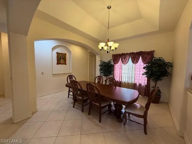 Dining area with a notable chandelier, a raised ceiling, and light tile patterned floors