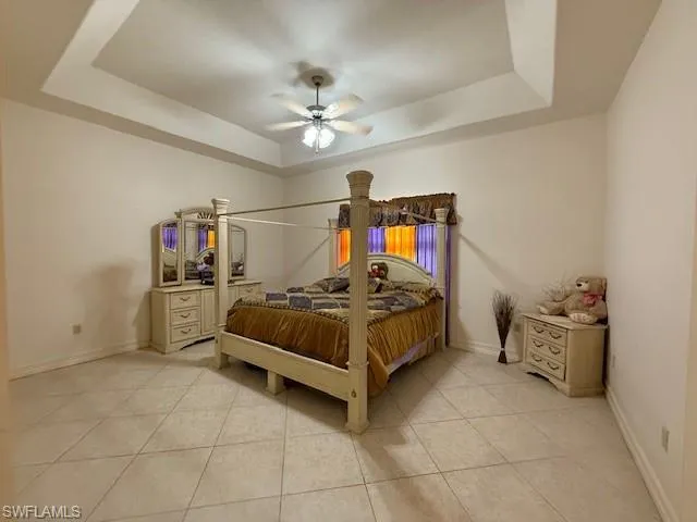 Bedroom with a tray ceiling, ceiling fan, and light tile patterned flooring