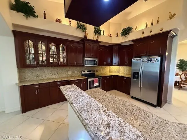 Kitchen with appliances with stainless steel finishes, a towering ceiling, tasteful backsplash, and light tile patterned floors