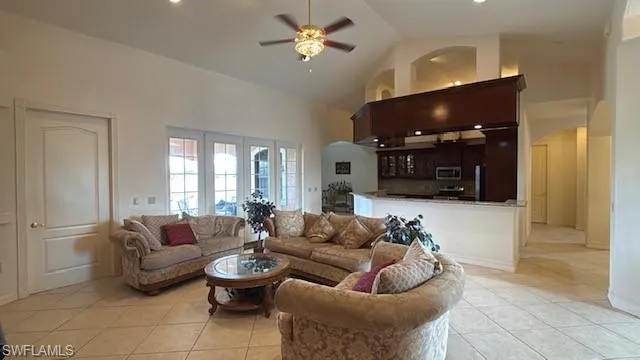 Living room featuring light tile patterned floors, high vaulted ceiling, and ceiling fan