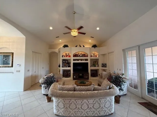 Living room with built in shelves, light tile patterned flooring, lofted ceiling, and ceiling fan