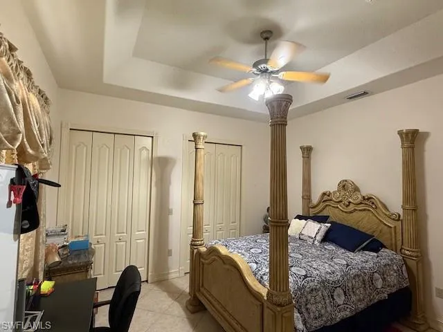 Bedroom with ceiling fan, a raised ceiling, and two closets