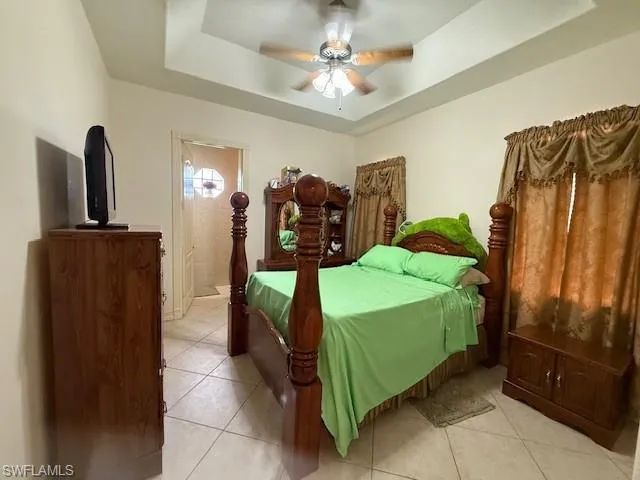 Bedroom with light tile patterned floors, connected bathroom, a raised ceiling, and ceiling fan