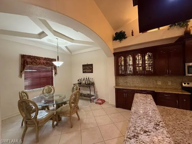 Bar featuring dark brown cabinetry, hanging light fixtures, stainless steel appliances, decorative backsplash, and light tile patterned flooring