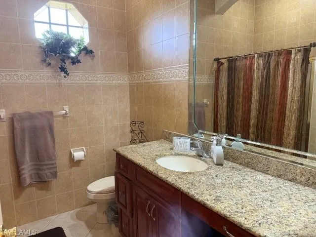 Bathroom featuring a shower with shower curtain, tile patterned floors, vanity, tile walls, and toilet